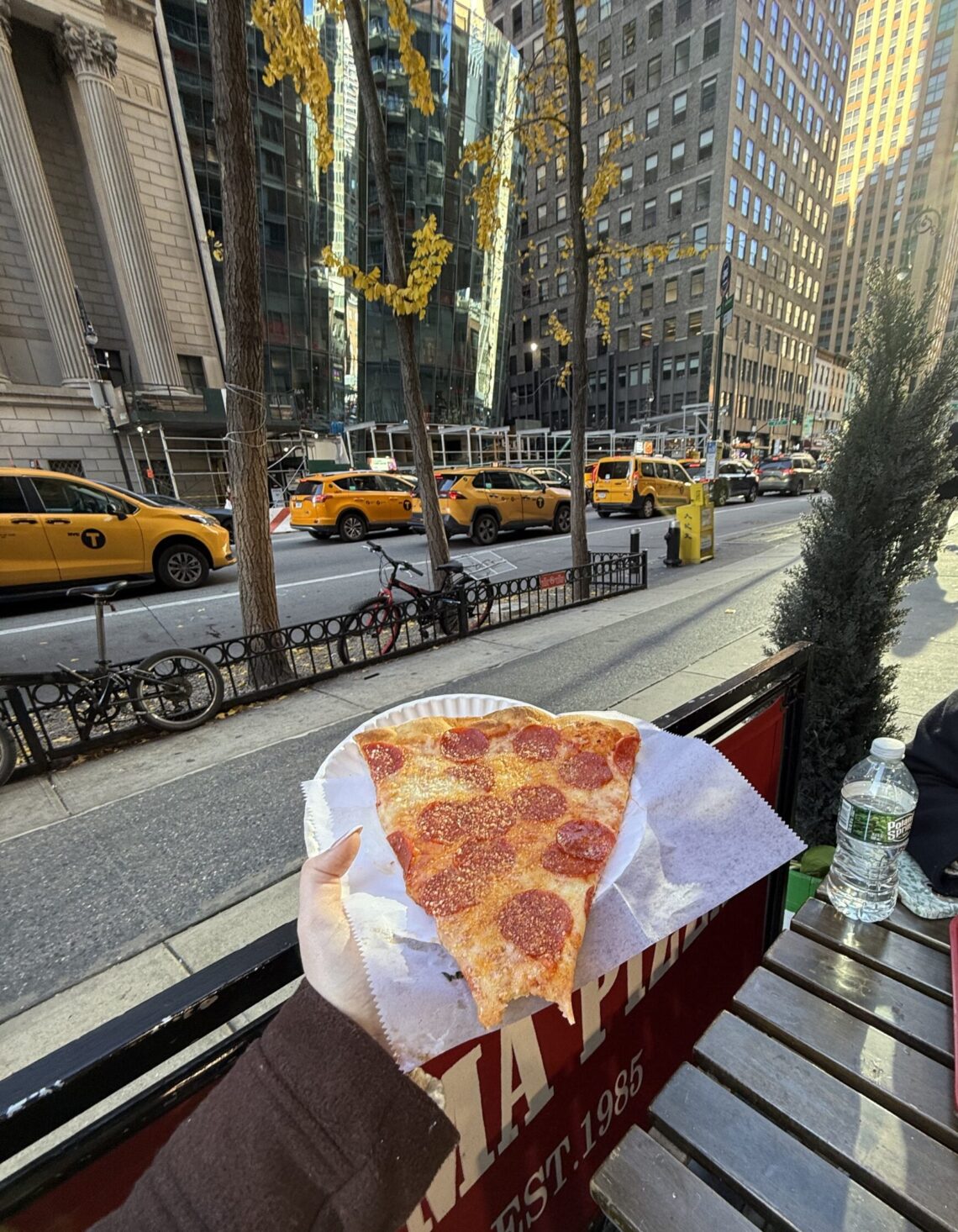 Holding up a slice of pizza in front of New York buildings and New York traffic