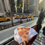 Holding up a slice of pizza in front of New York buildings and New York traffic