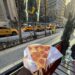 Holding up a slice of pizza in front of New York buildings and New York traffic